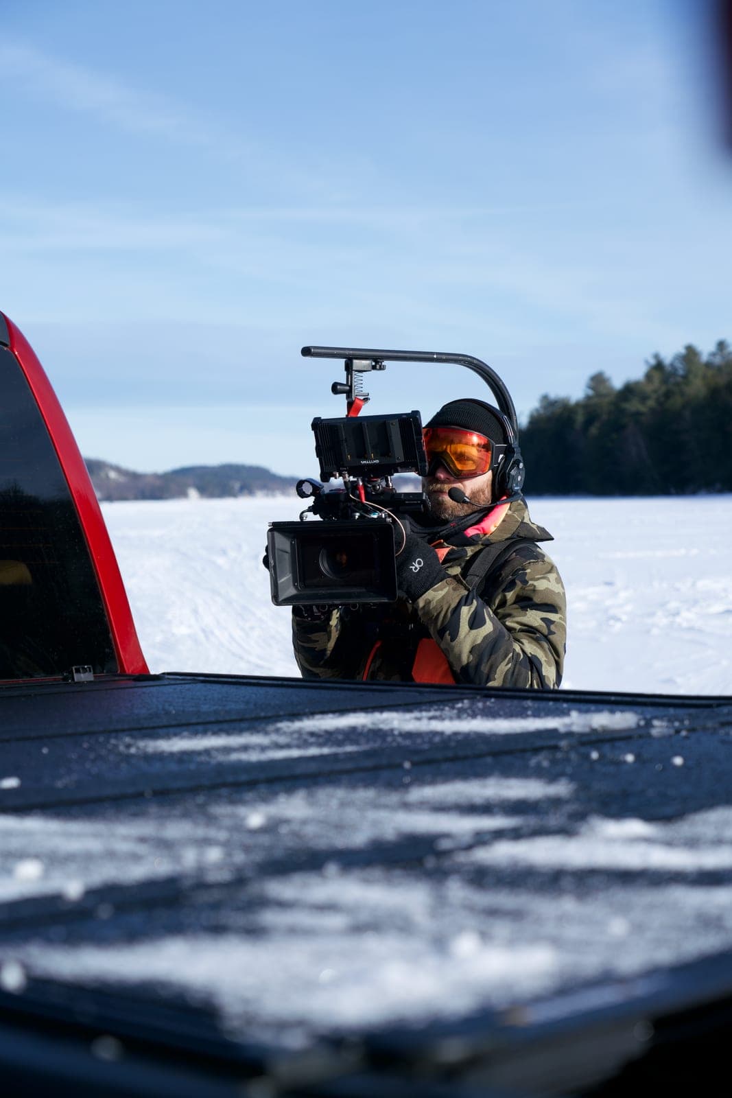 An operator shooting from the bed of a truck out across a frozen lake, camera braced on the tailgate