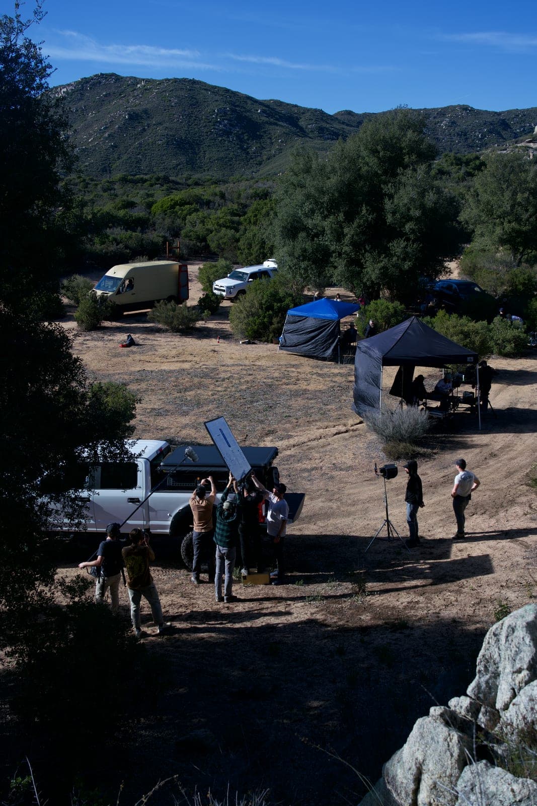 A wide of the whole unit on location: video village under tents, vehicles along the track and the camera team building a setup below