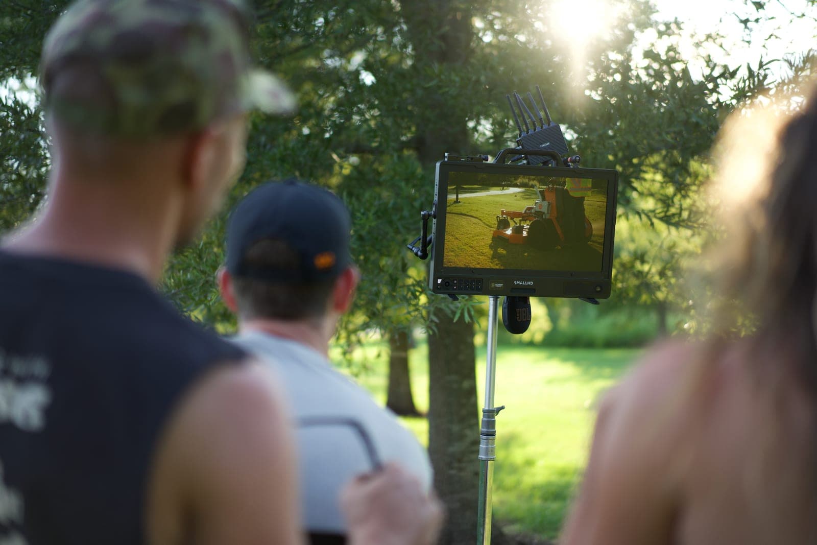 Three of the crew watching a monitor on a stand, the shot on screen showing a mower moving through dappled light