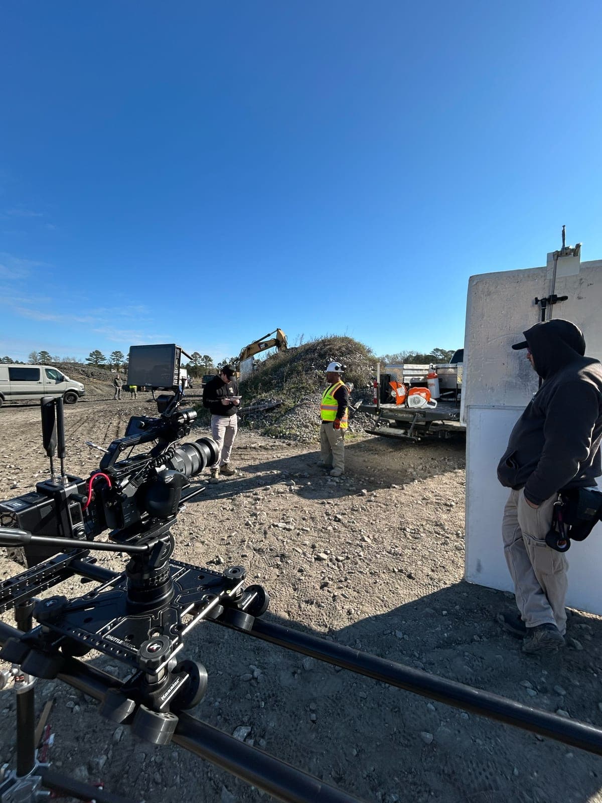 A camera on a jib arm at a quarry, an excavator working the pile behind and crew in high-visibility vests around it